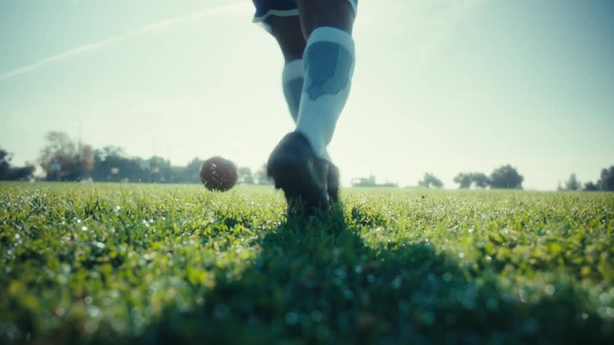 A soccer player practices on a lush green field under the sunny sky