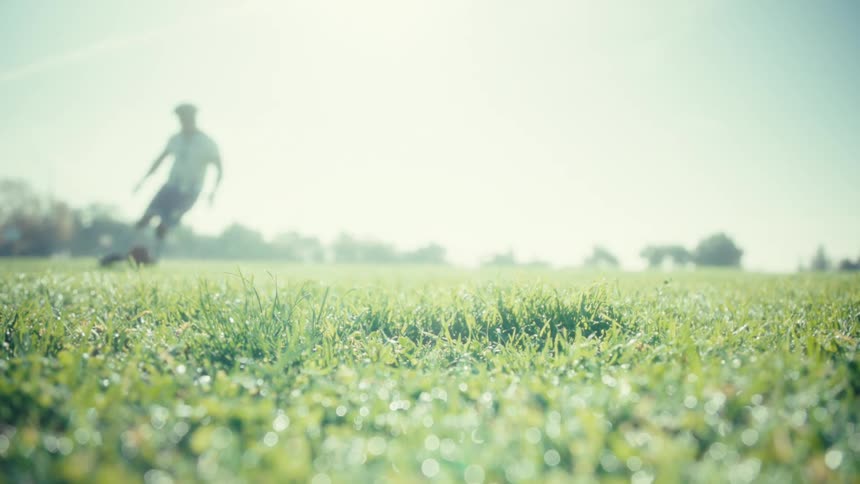 A soccer player kicks a ball across a sunny grass field moving with energy and control under the bright daylight