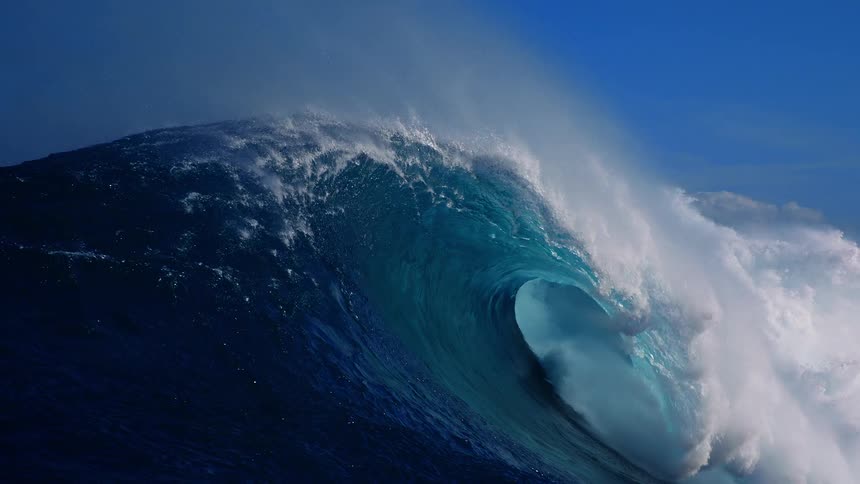 Large wave breaks creating foaming water under a bright blue sky