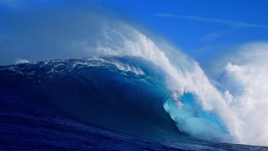 Heavy waves rise and roll across the ocean on a sunny day crashing powerfully into the water as bright light glints off the surface