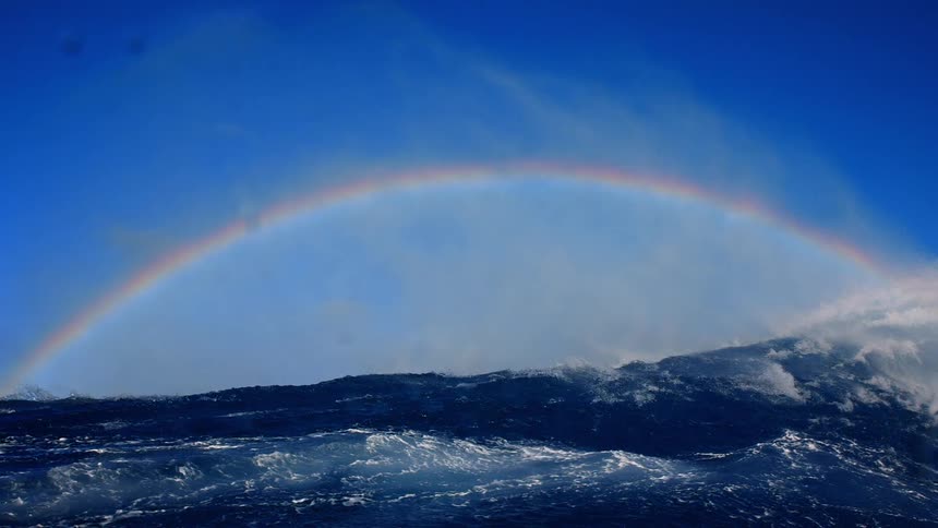 Rainbow in a blue sky over a turbulent sea
