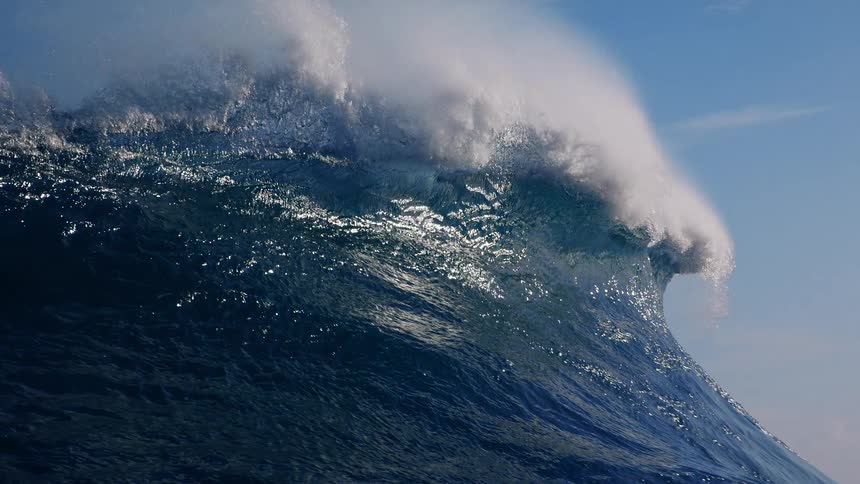 Sunlight shines on a huge wave splashing and curling as it rolls in to shore