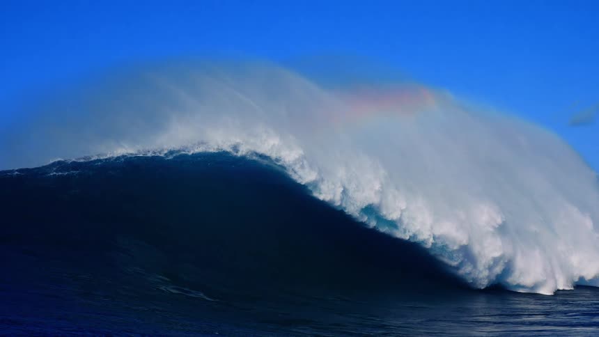 Sunlight shines on a huge wave splashing and curling as it rolls in to shore