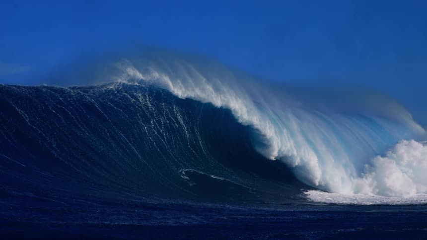 Sunlight shines on a huge wave splashing and curling as it rolls in to shore