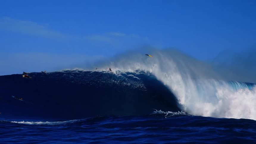 People on surfboards ride over a huge wave splashing and curling as it rolls into shore