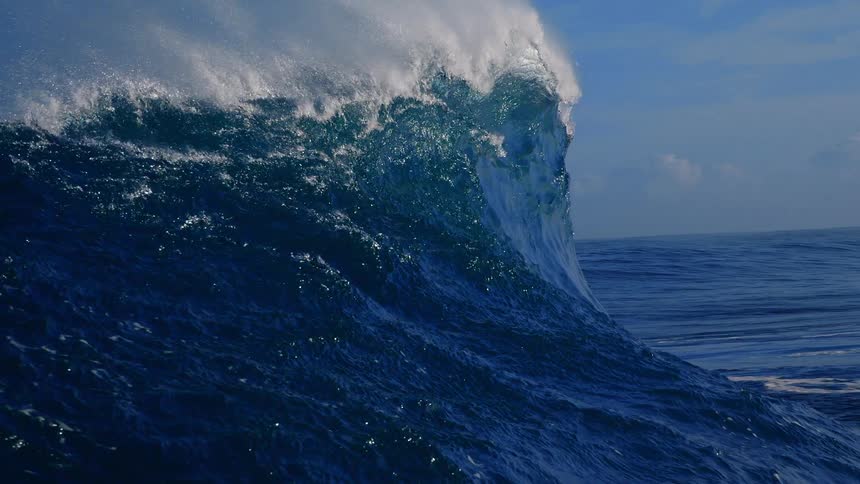 Large wave breaks under a cloudy sky during the daytime