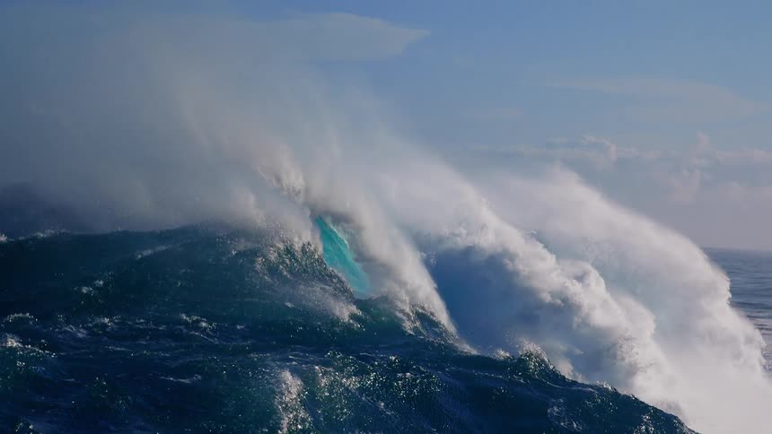 A powerful teal wave curls into a barrel before collapsing into heavy whitewater and mist while the camera moves through the deep blue surface of the open ocean under a clear sky