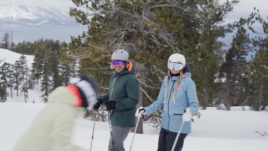 Four skiers in winter gear laugh and chat atop a snowy mountain slope