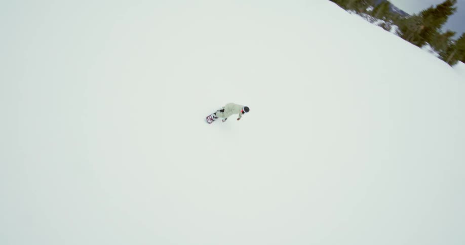 A person rides a snowboard down a snowy mountain at midday carving through the bright sunlit slopes with speed and control