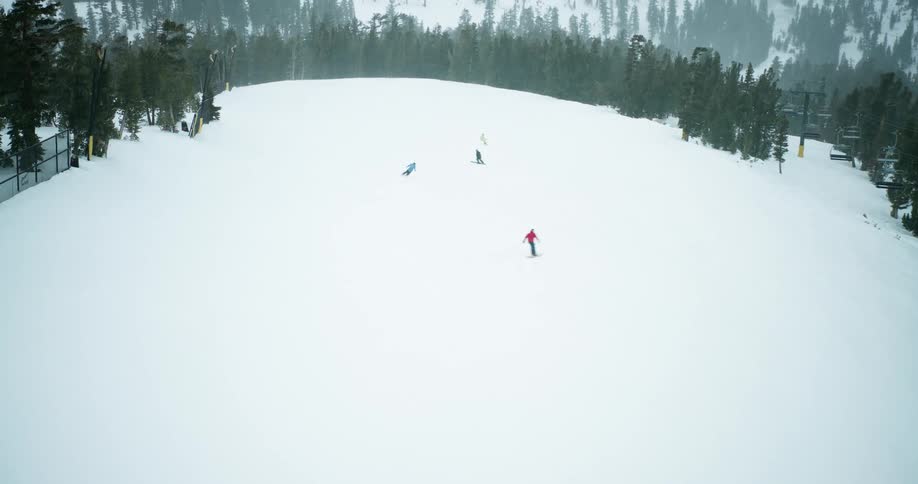 Aerial view of a skiers descending a snow covered mountain slope past a chairlift and evergreen trees