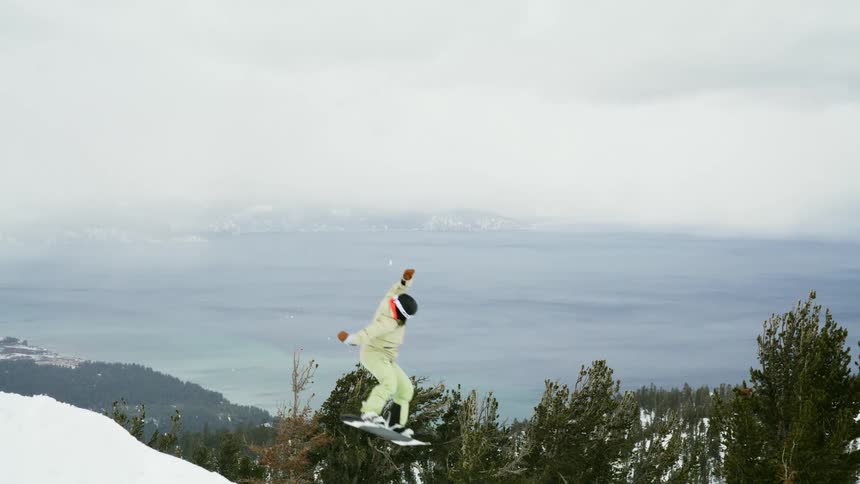 A snowboarder jumps off a snowy mountain slope with a forest and distant landscape behind