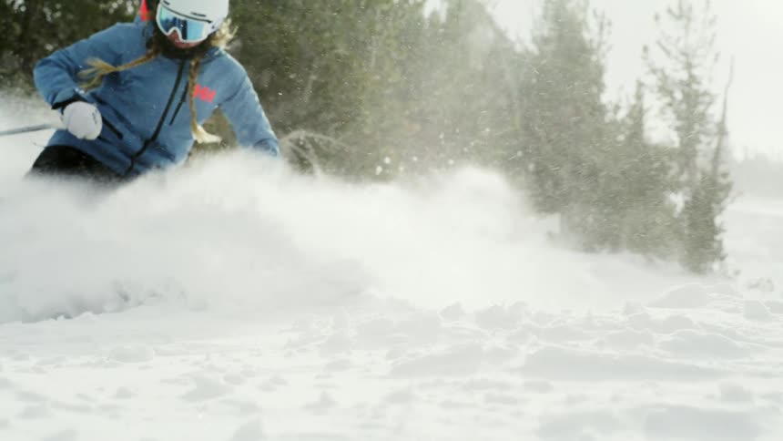 Snow falls as a skier turns near trees and snow flies into the air