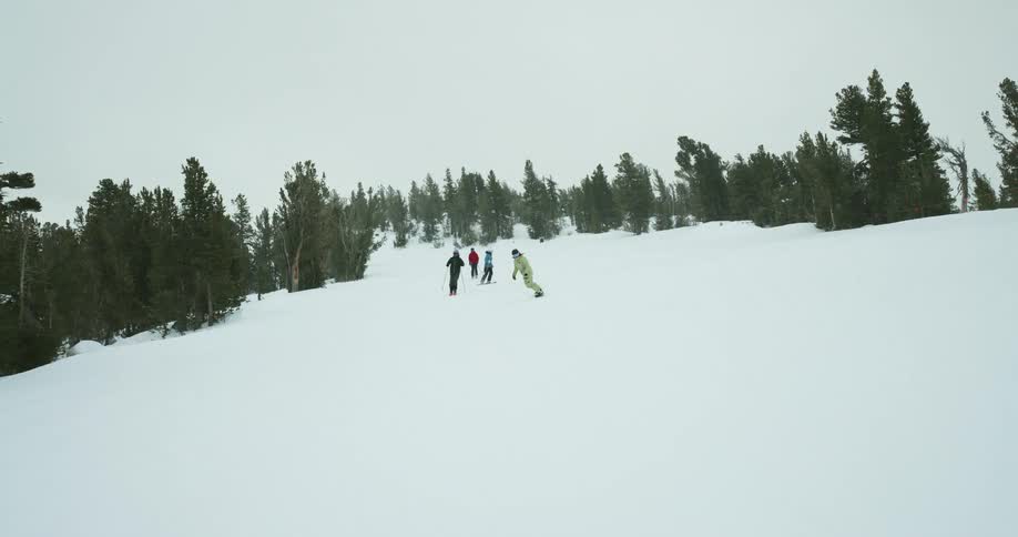 Three people skiing and one snowboarding in the snowy mountains