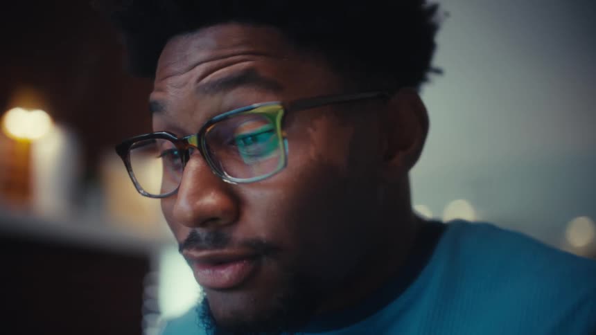 Man smiles as his glasses reflect the screen of the computer he is using