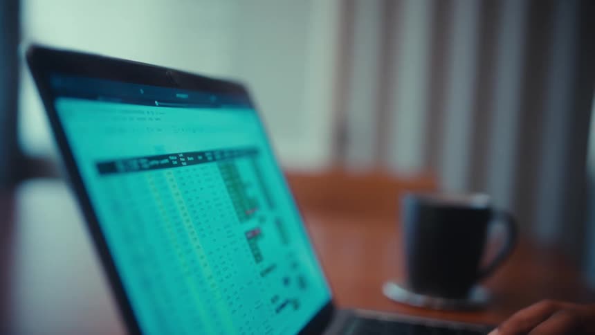 Man sitting at a table typing on the keyboard of a laptop computer