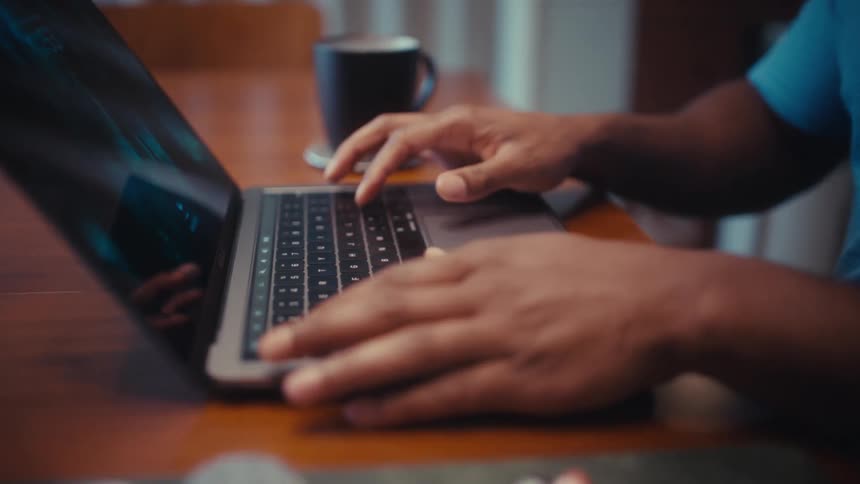 A man works on a laptop at a wooden desk in a bright modern room