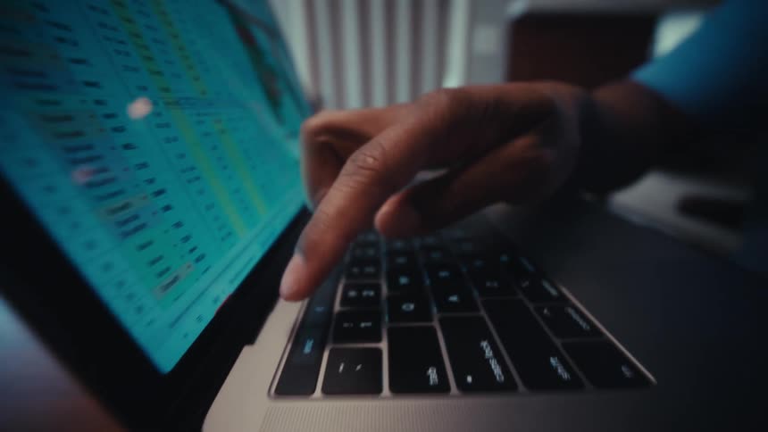 Man sitting at a table typing on the keyboard of a laptop computer