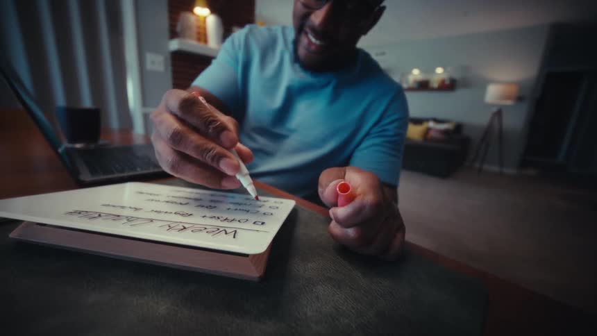 A person checks off items on a weekly checklist at a desk indoors