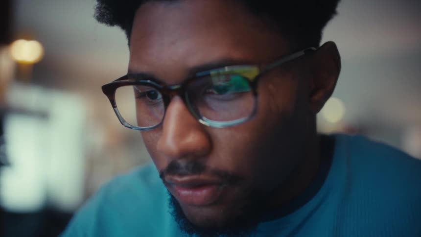 Close up of a young black man working with a laptop computer while sitting at a table indoors during daytime