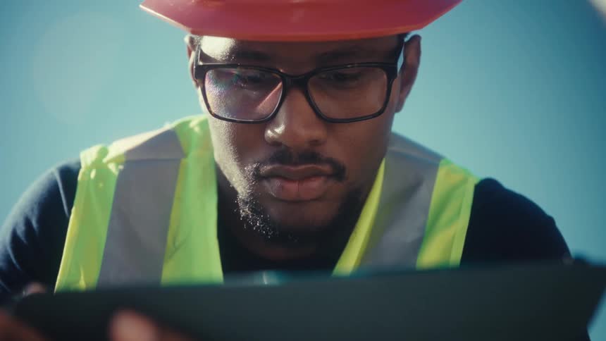 A male engineer checks a tablet while working on an outdoor construction site