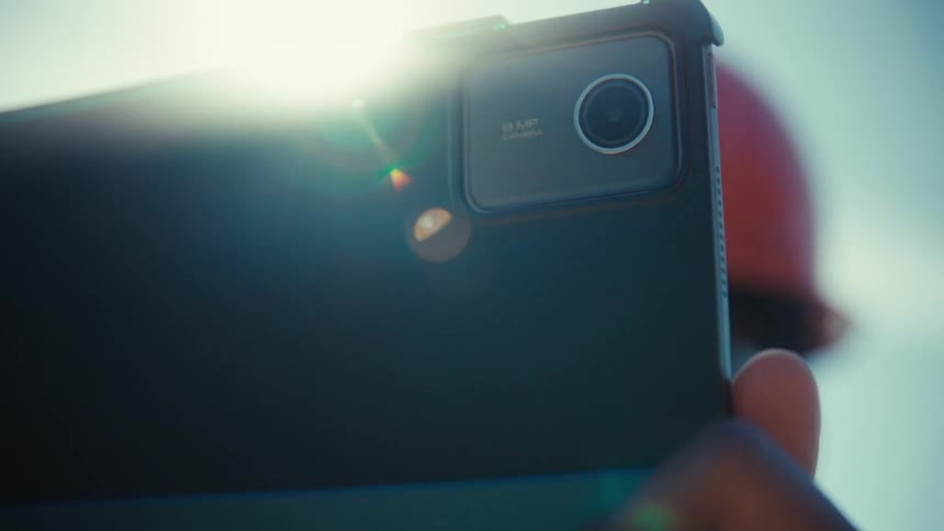 An engineer holds up a tablet its surface washed out by a bright flaring sun