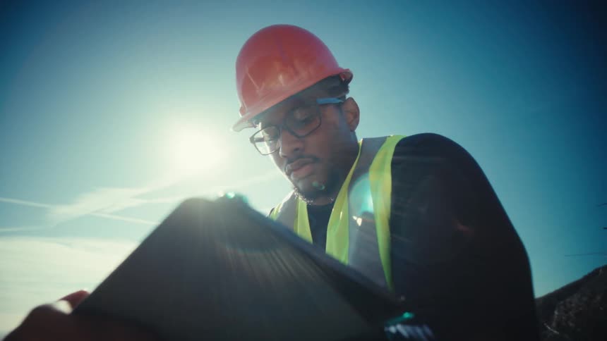 An industrial engineer checks a tablet at an outdoor job site in sunlight