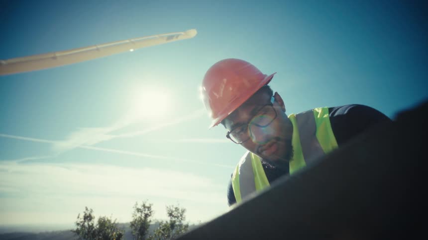 A male technician checks a tablet under a wind turbine at a windfarm in daylight
