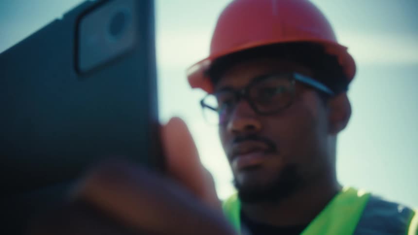 An engineer in a hard hat holds a tablet with the view shifting from the device to his focused expression
