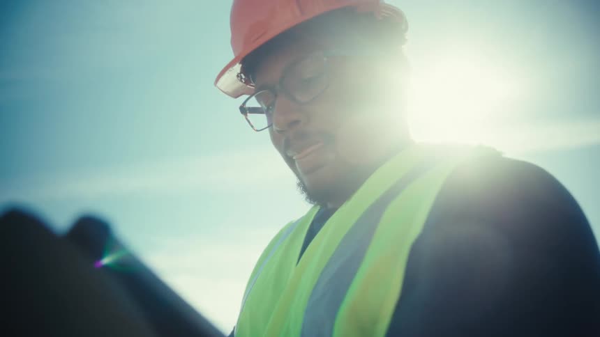 An engineer in a hard hat focused on his work backlit by the bright sun