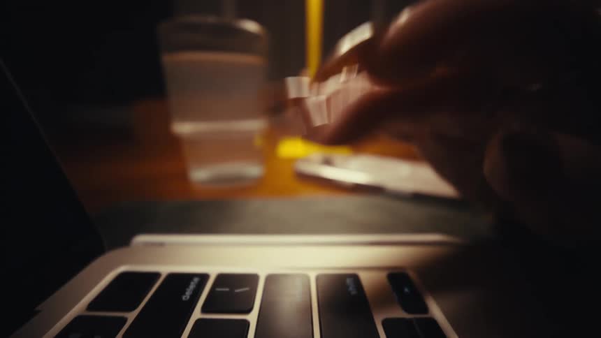 A womans finger types on a laptop keyboard a glass of water sitting beside it on the table as a lamp brightens the scene with warm light
