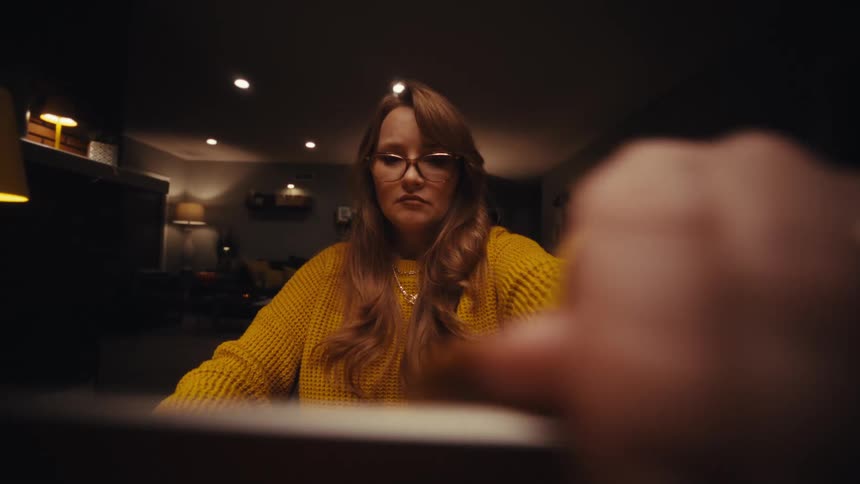 A young woman opens her laptop computer to work while sitting at a table indoors at night