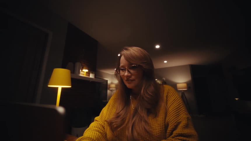 Close up of a young woman working with a laptop computer while sitting at a table indoors at night