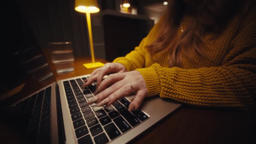 Woman with long fingernails types on the keyboard of a laptop computer