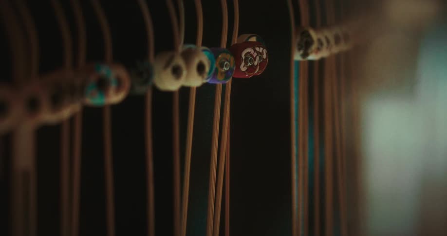 The video shows a closeup shallowdepthoffield shot of several thin vertical brown lines that appear to be wooden sticks or incense threaded onto one of these lines is a row of small colorful decorative beads including a prominent red bead with a