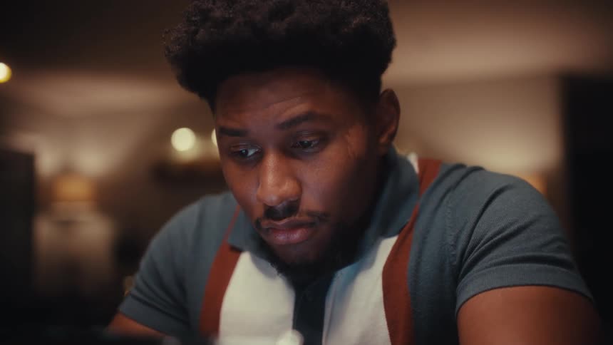 Close up of a young black man using a tablet computer while sitting at a table indoors at night