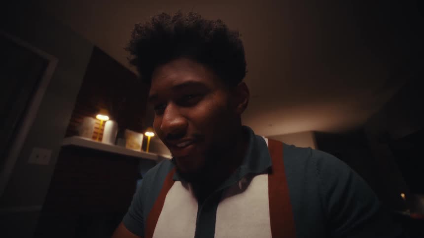 Close up of a young black man typing while using a tablet computer as he is sitting at a table indoors at night