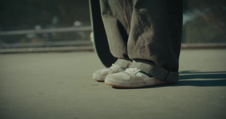 Person standing on a park stomping on a skateboard and picking it up outdoors during dusk or dawn