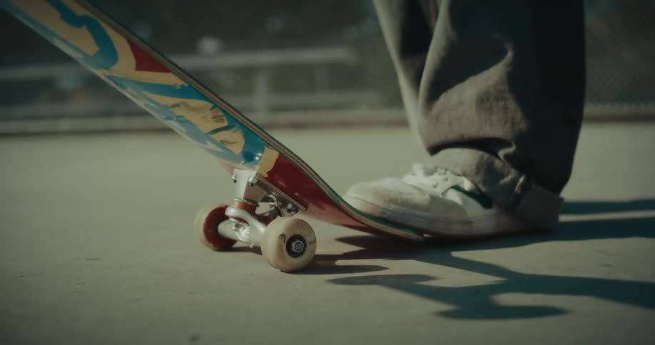 A person stands on a skateboard on a concrete floor at midday sunlight casting clear shadows across the ground