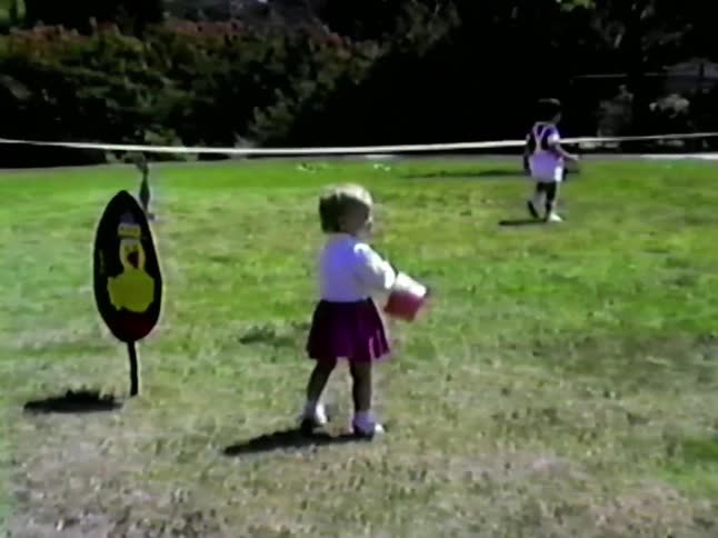 Two toddlers walk around a playground at midday exploring and playing as bright sunlight fills the area