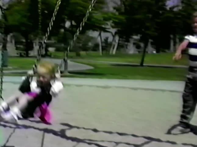 A teenage boy pushes a young girl on a playground swing at midday sunlight brightening the lively outdoor setting