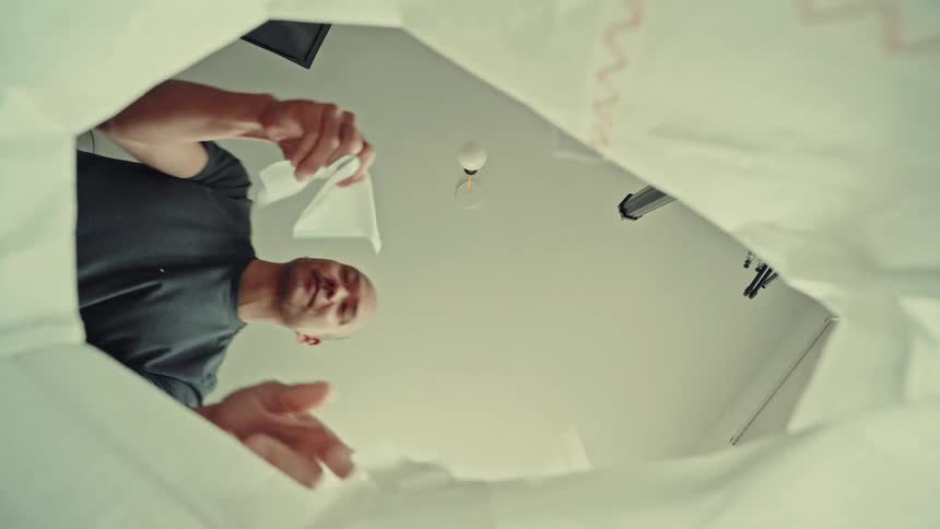 Young adult man opening a plastic bag and picking up a paper tissue on his hand indoors during day time