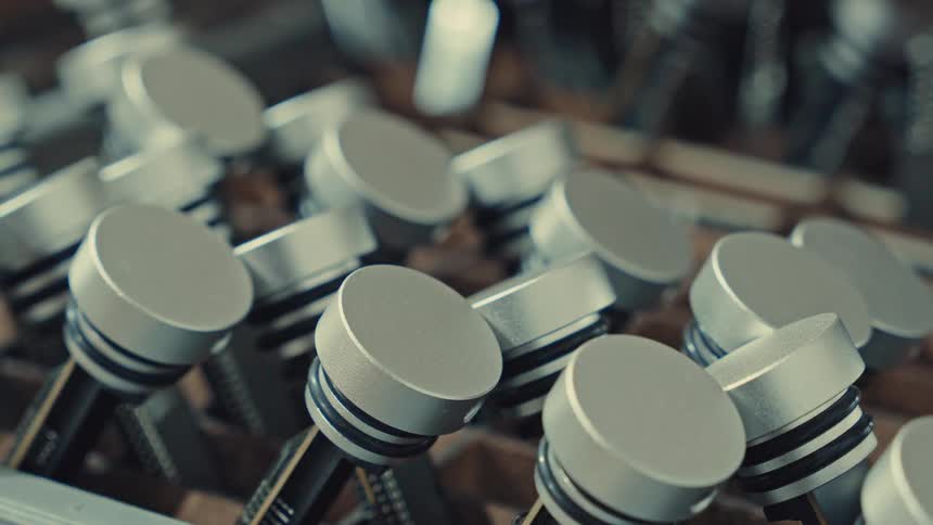 A series of pistons arranged neatly inside a box indoors at midday the metal components catching soft light from the room