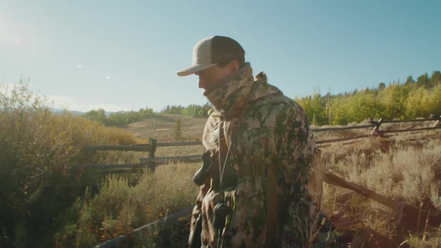 A man in a camouflage coat with a gun walks with his dog outdoors