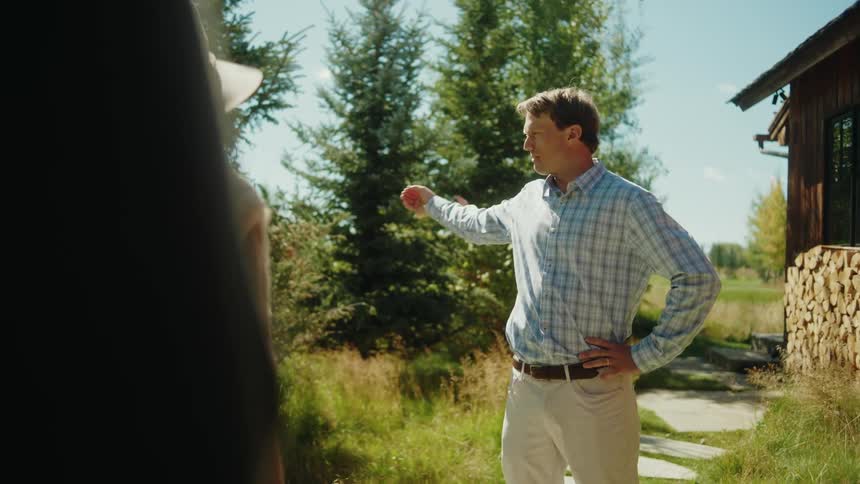 Two people stand on a lawn under the midday sun engaged in a relaxed conversation as bright light casts clear shadows across the grass
