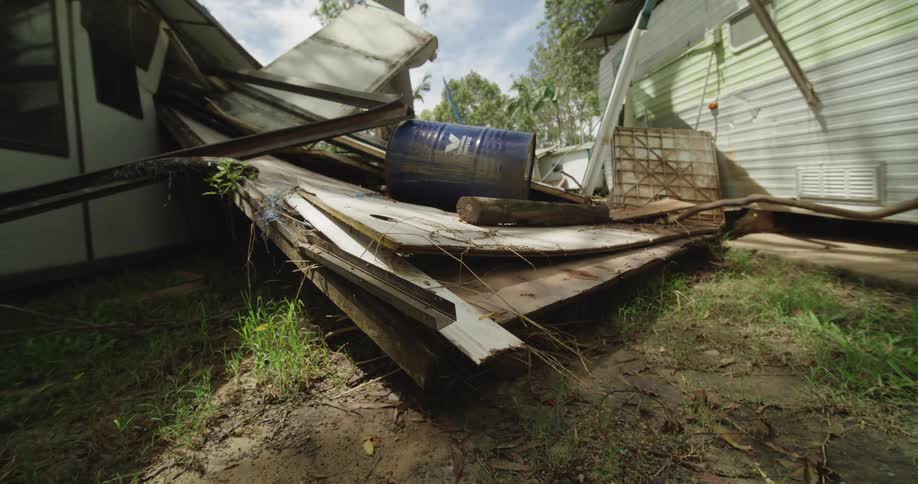 Steel barrel over pieces of broken wood next to a broken wooden house in a suburban area outdoors during day time