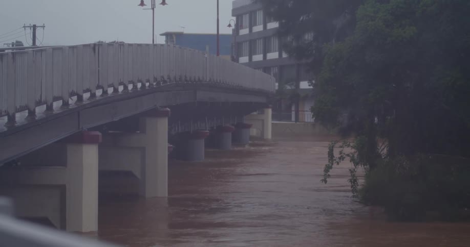 A flooded city at midday with water flowing beneath an overhead bridge