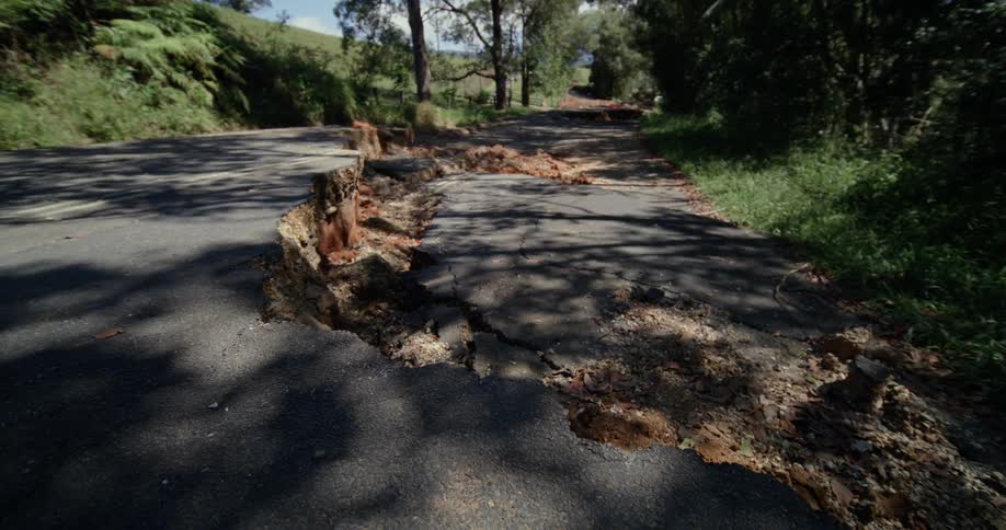 This video shows a paved road that has been severely damaged by a landslide or ground collapse large sections of the asphalt have buckled and dropped away creating deep fissures and making the path completely impassable for vehicles