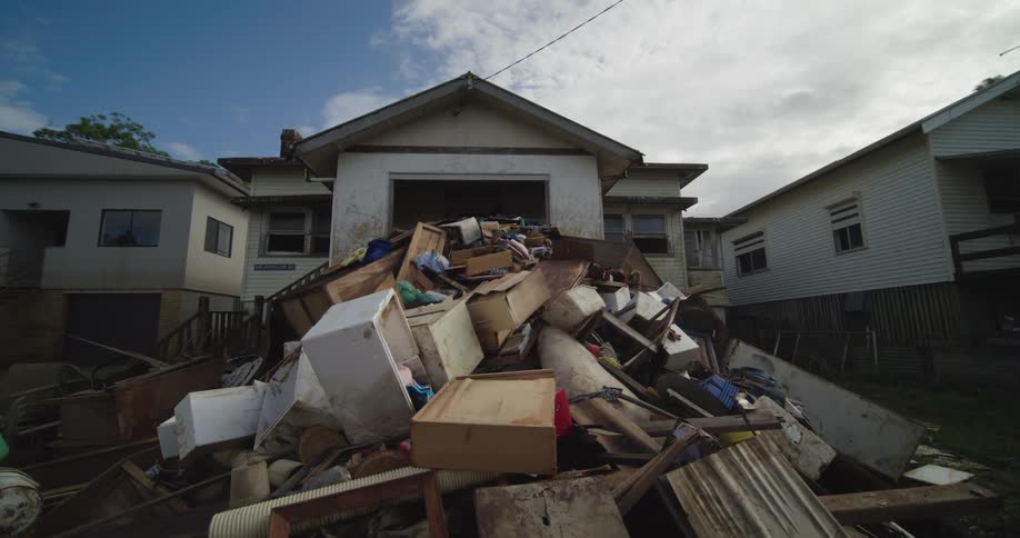 A residential neighborhood at midday with a building that has a pile of discarded furniture and trash set out in front of it