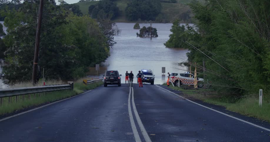 The police car is parked on the road by the flooded river