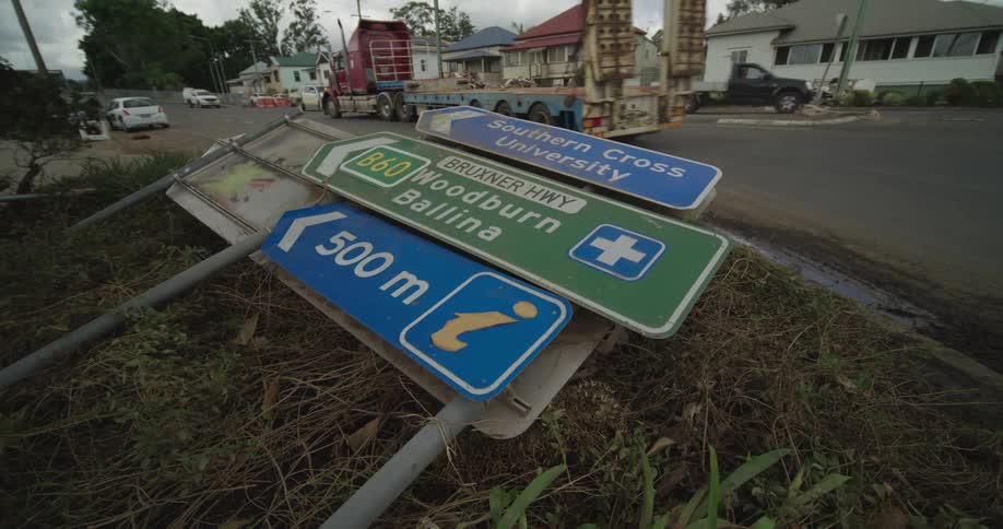 The four signs are laying on the ground beside a busy road and the cars suvs trucks and a semi are just going down the road beside of it